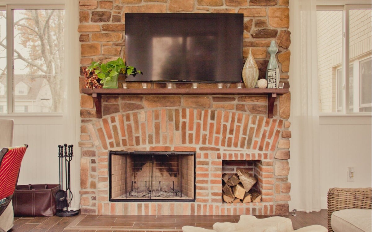 Brick fireplace with log storage and mounted TV in Cincinnati sunroom addition by Legacy Builders