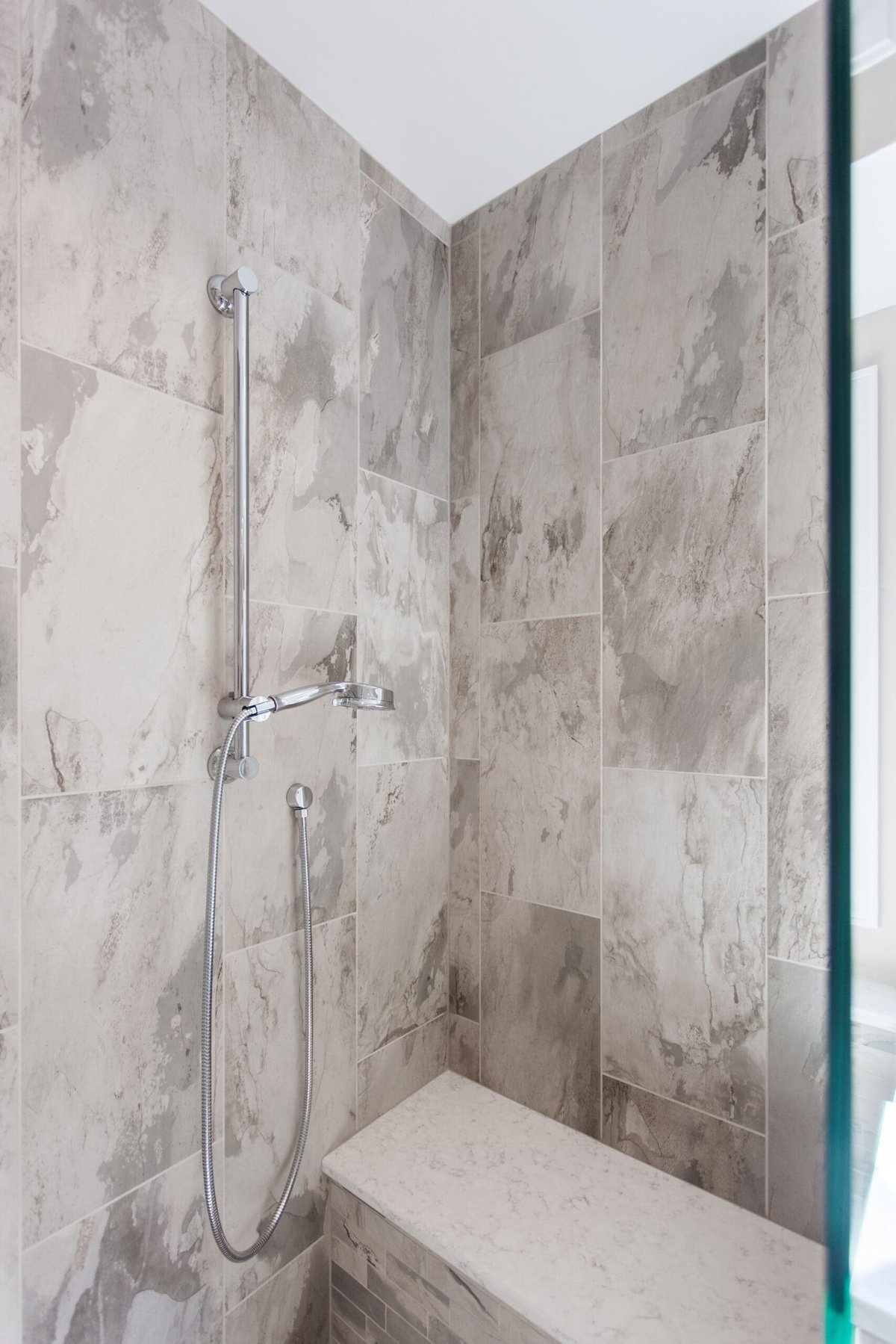 Chrome grab bar and shower head next to built-in shower bench in accessible bathroom remodel by Legacy Builders