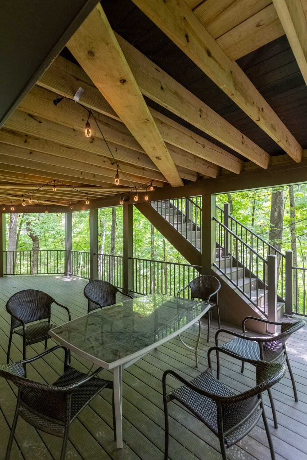 Lower-level covered outdoor living area with string lights and a staircase by Legacy Builders in Cincinnati