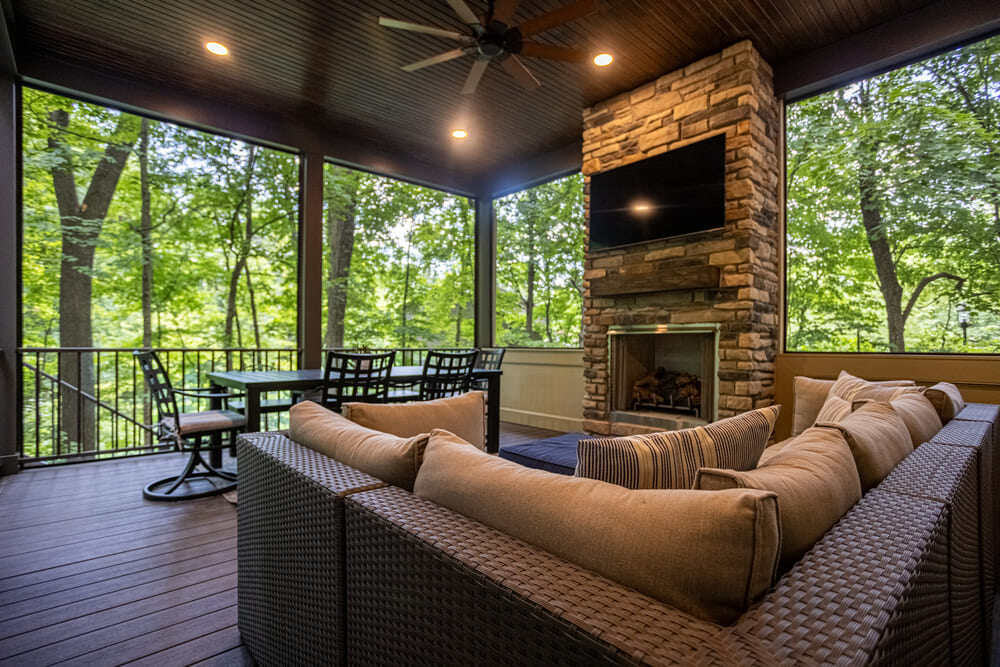 outdoor living space with a stone fireplace and TV in a screened-in porch by Legacy Builders in Symmes Township, Ohio